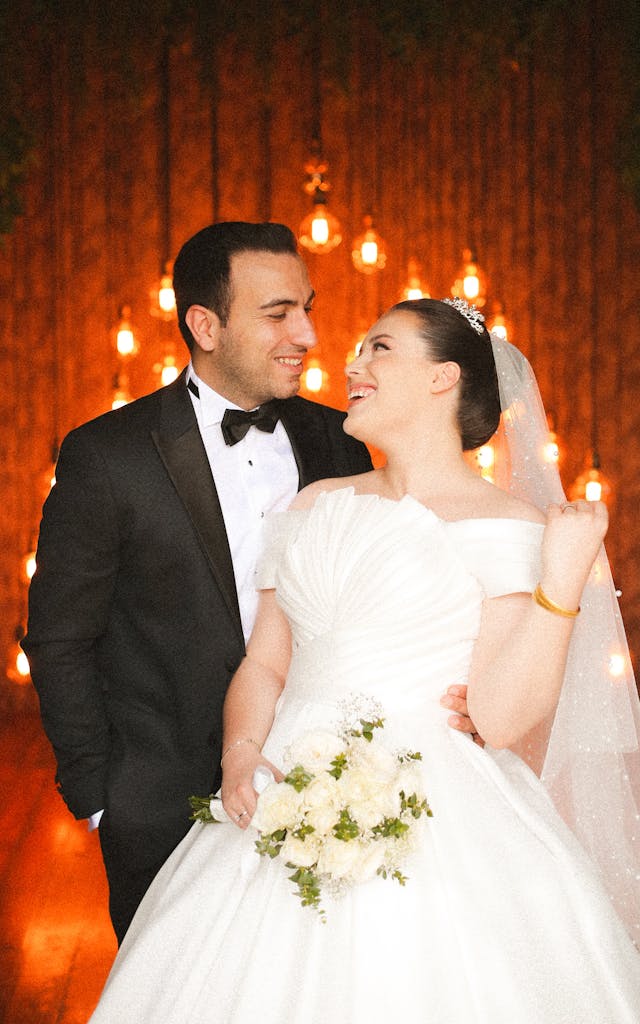 A bride and groom pose for a photo in front of a lit up wall